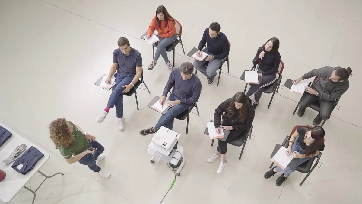 Un corso in aula visto dall'alto: gli allievi ai banchi e la docente accanto ai dispositivi di protezione